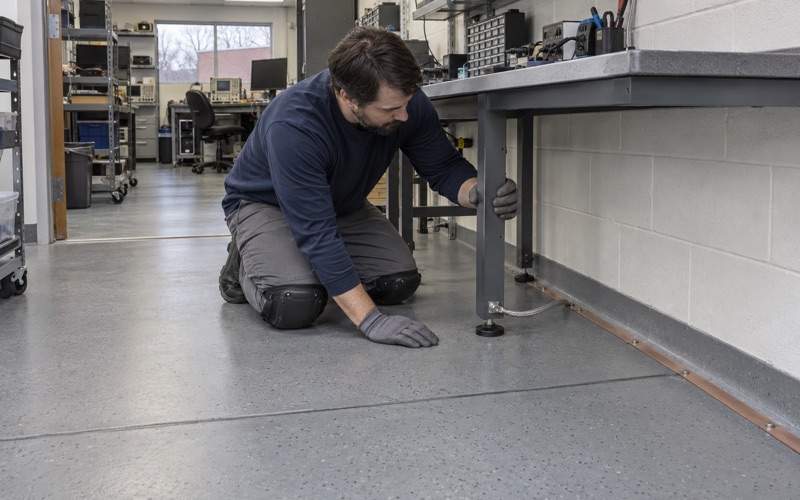 A static-dissipative floor with a copper grounding strip under an electronics repair bench in a Wheaton flex building.
